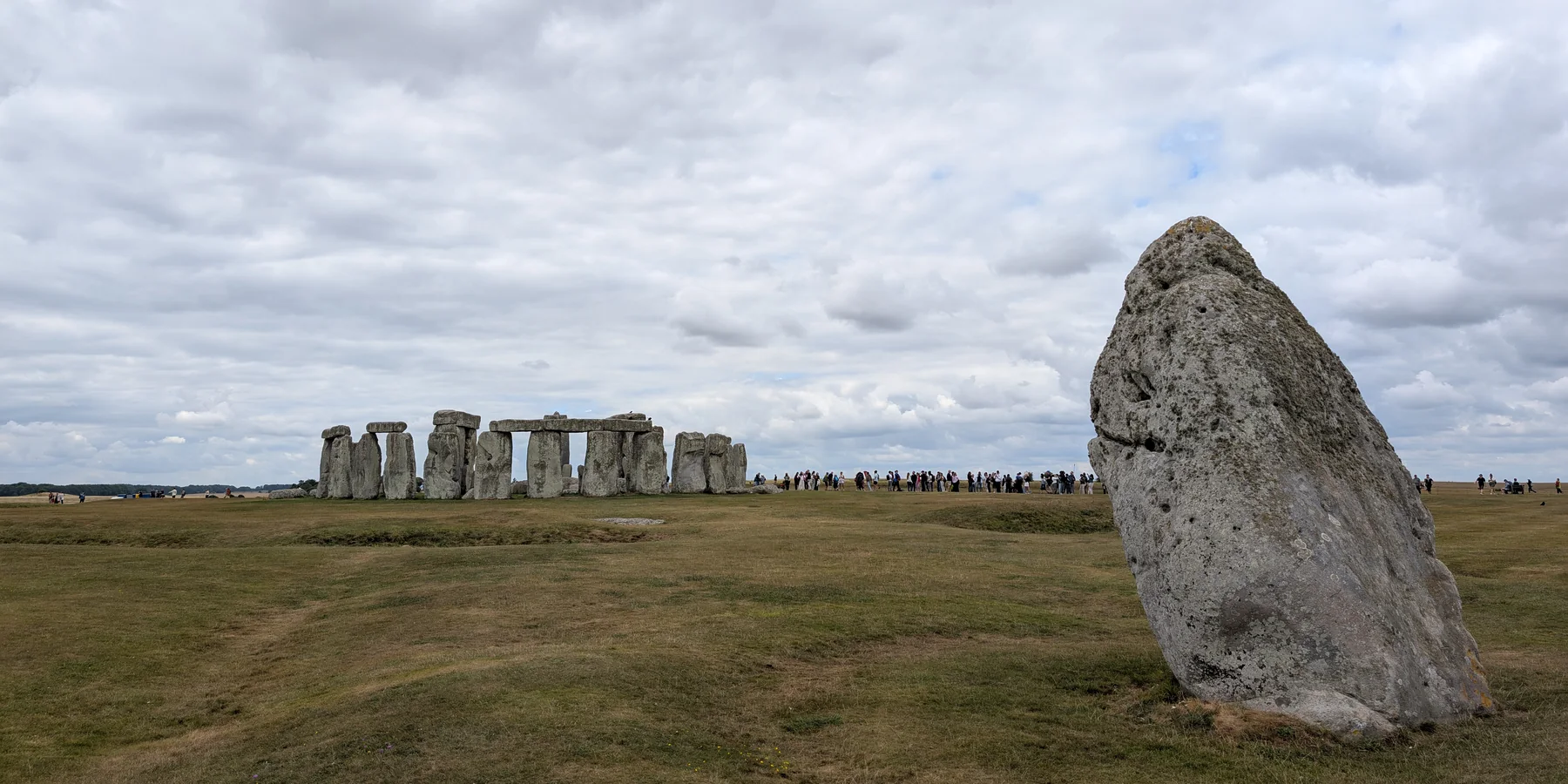 Kámen Heel Stone v popředí ve Stonehenge, za ním kamenný kruh a dav denních návštěvníků